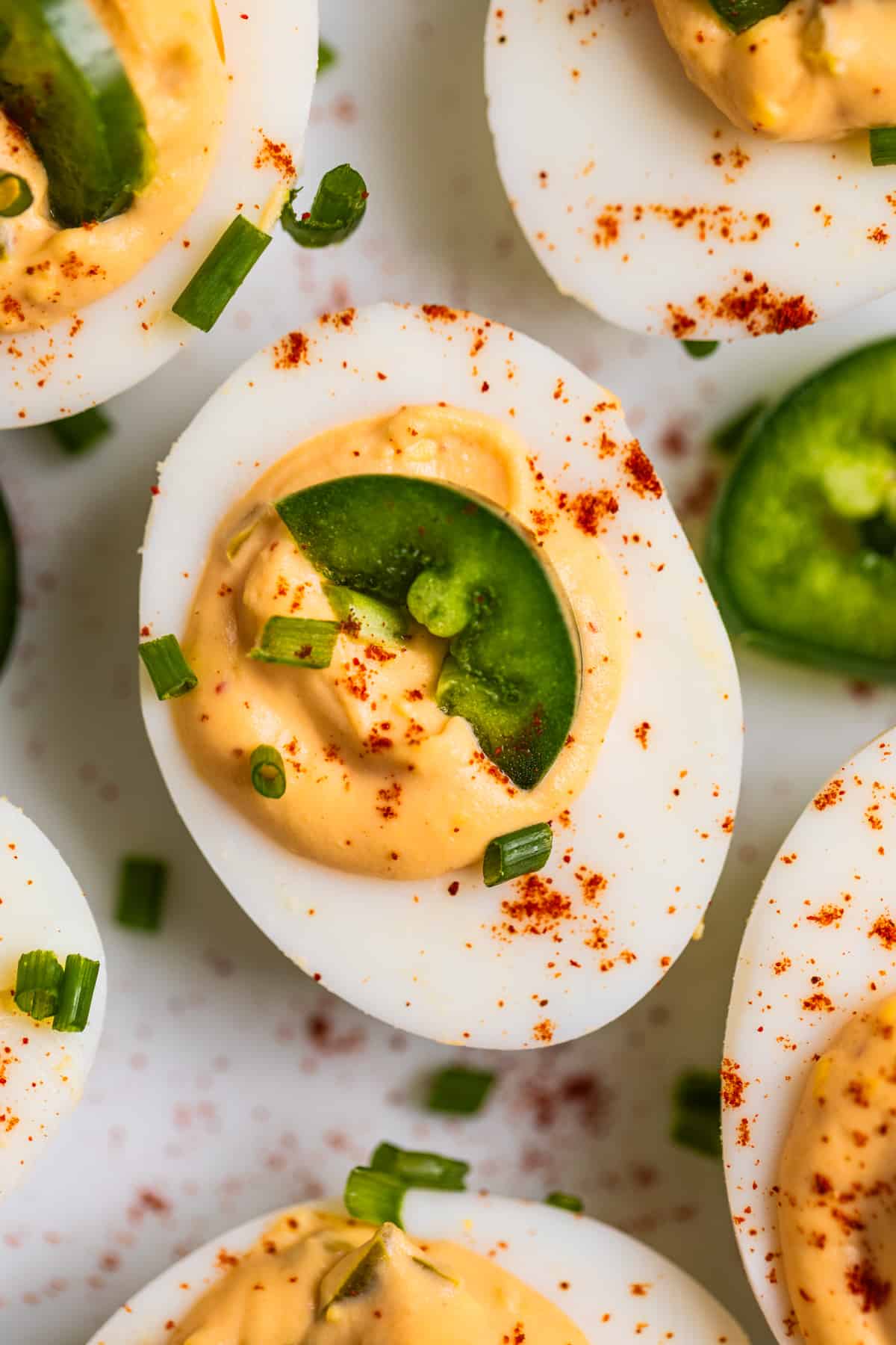 Close up view of spicy deviled egg on plate with slice of jalapeño and paprika on top.