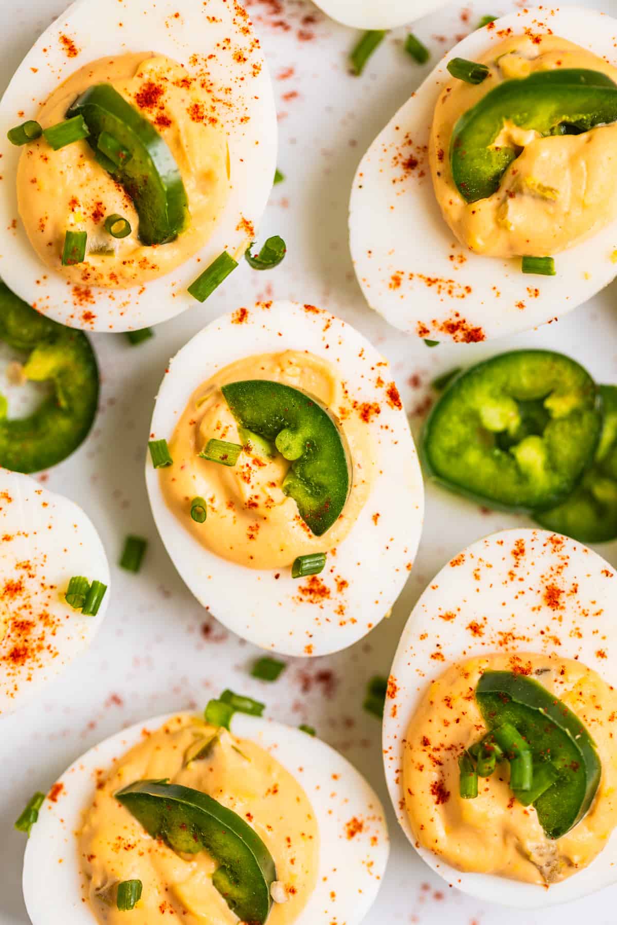 White dish with spicy deviled eggs topped with half slice of jalapeño and a sprinkle of paprika and chives.