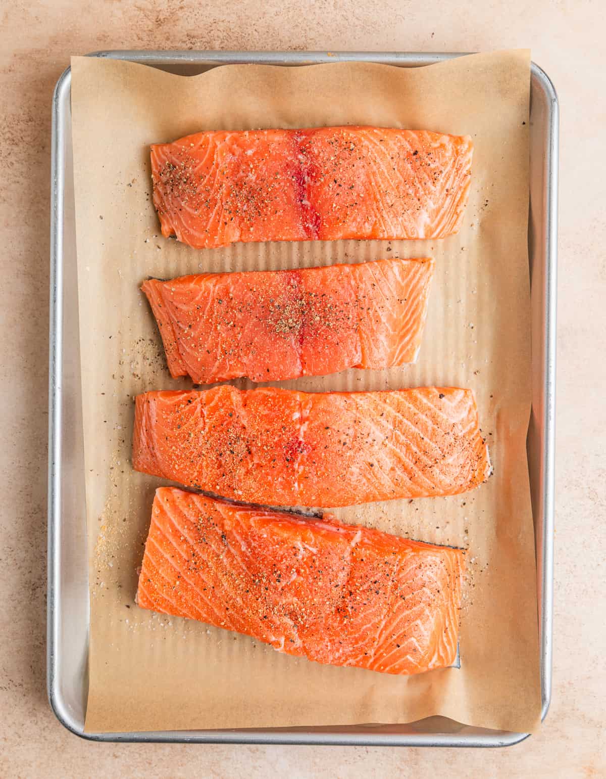 Raw salmon filets on parchment lined pan with seasoning.