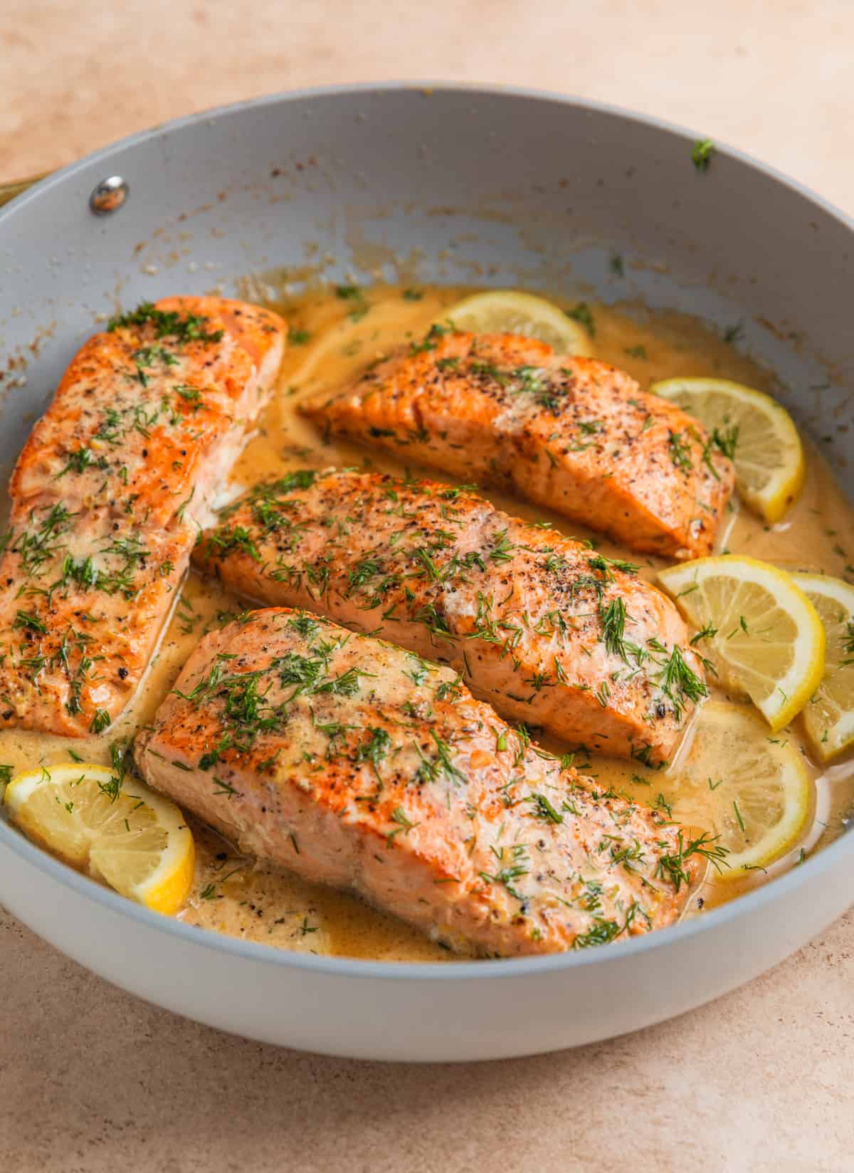 Cooked lemon dill salmon in pan with lemon slices and butter sauce.