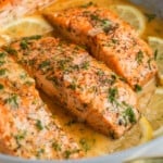 Lemon dill seared salmon in skillet with extra chopped dill on top and lemon slices.