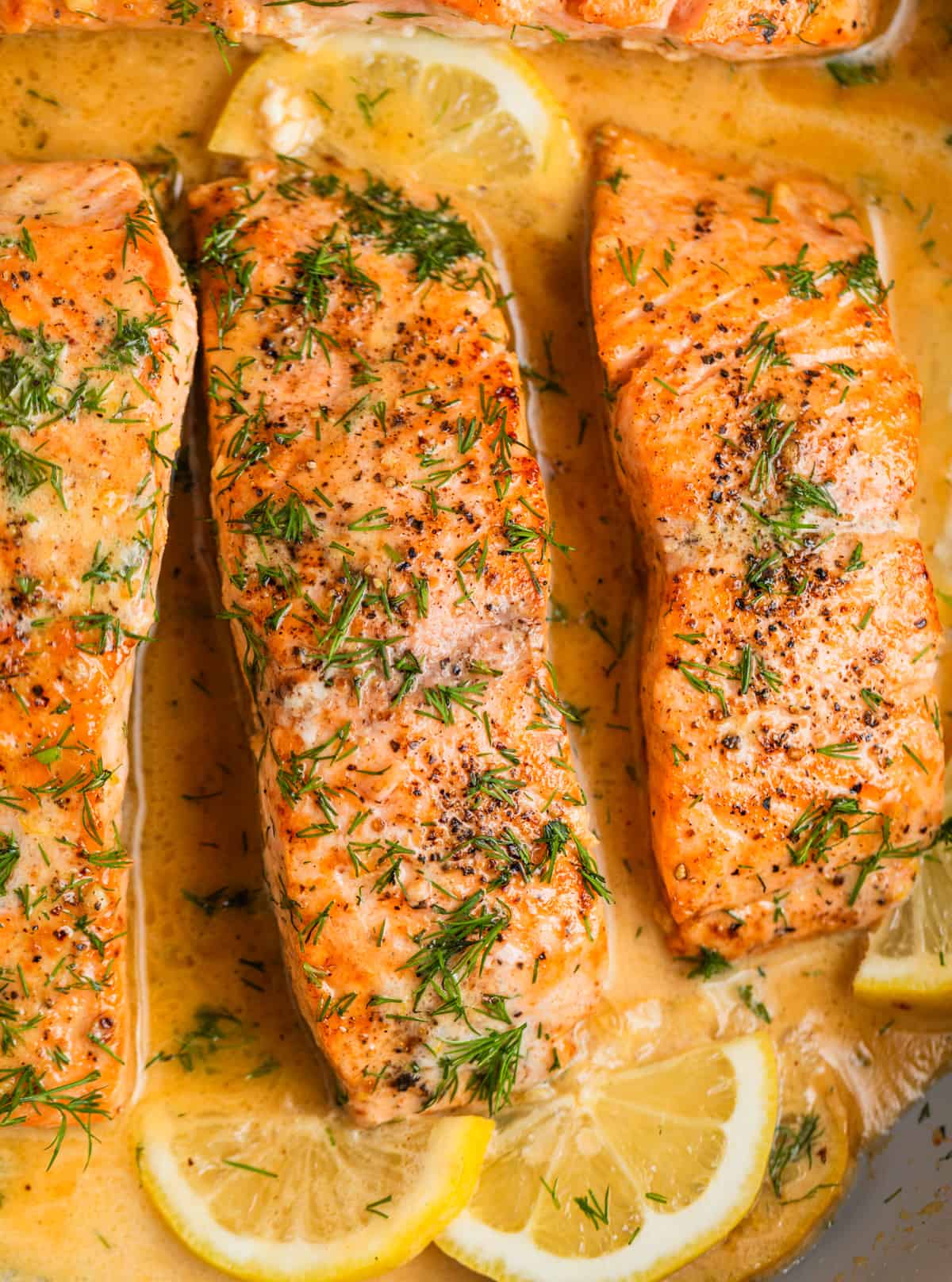 Overhead view of pan seared salmon fillets topped with fresh dill and lemon slices in pan.