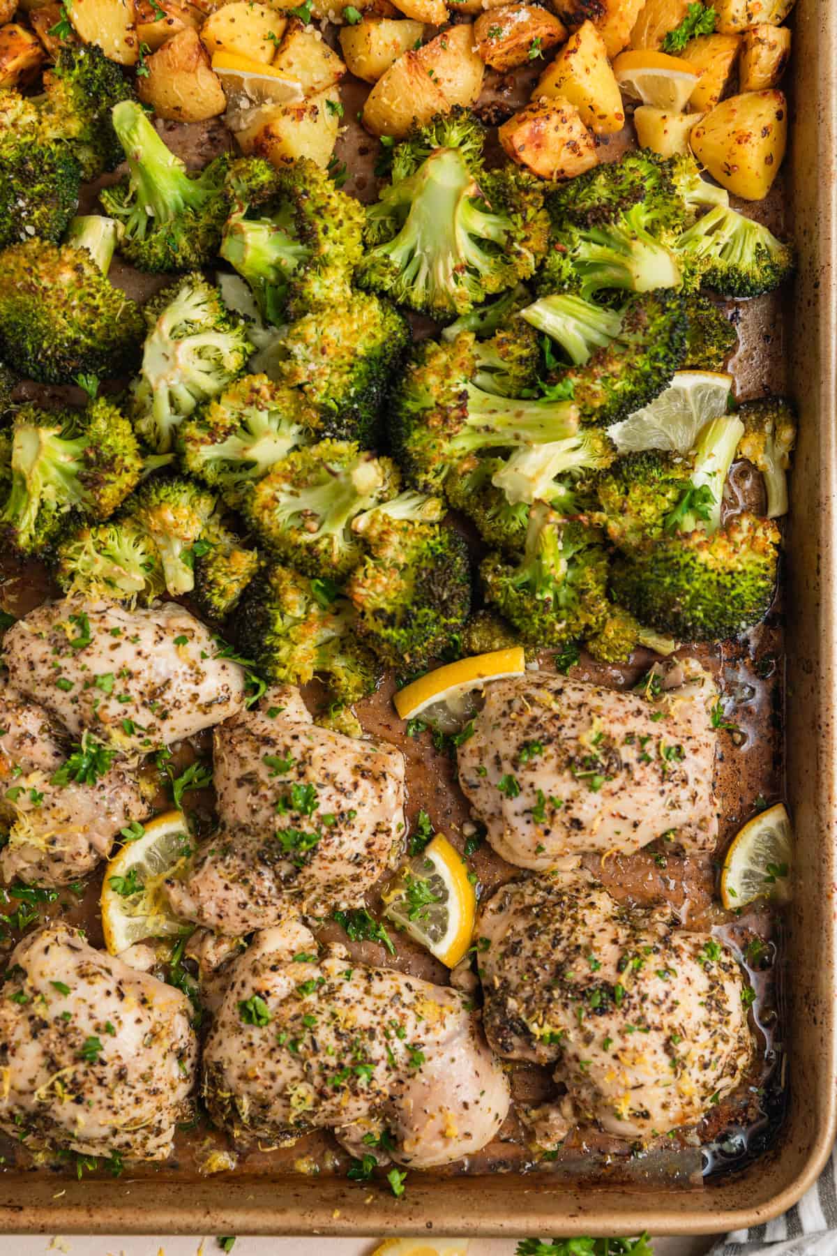 Sheet pan with cooked lemon chicken thighs, broccoli and quartered potatoes with chopped parsley.