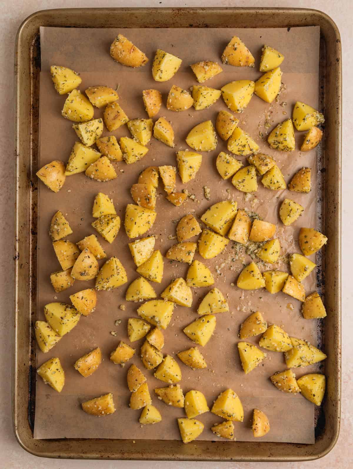 Parmesan, oil and herbed potato pieces lined on sheet pan.