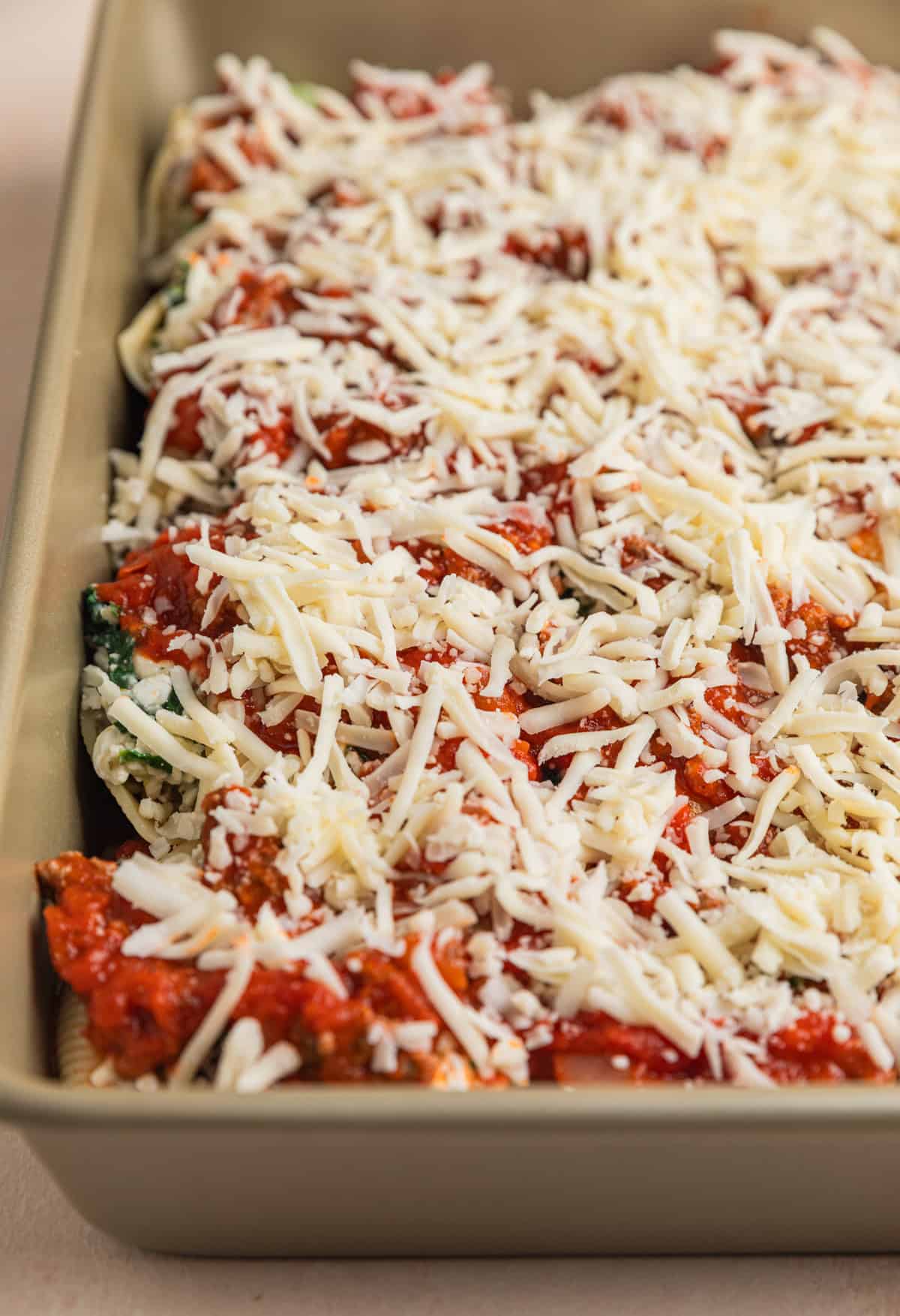Shredded mozzarella cheese sprinkled over top of shells with ground beef in baking pan.