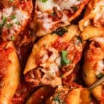 Ground beef stuffed shells in marinara with cheese and chopped basil over top.