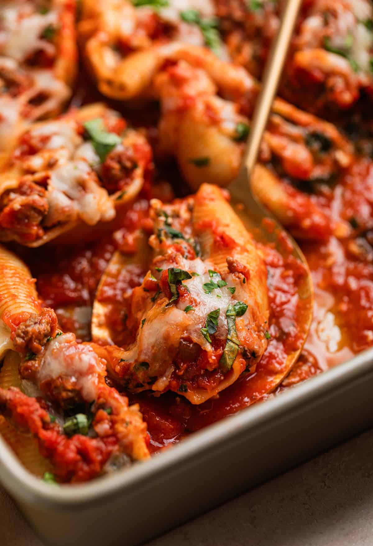Spoon with beef stuffed shell on it topped with melted cheese and chopped parsley and basil.