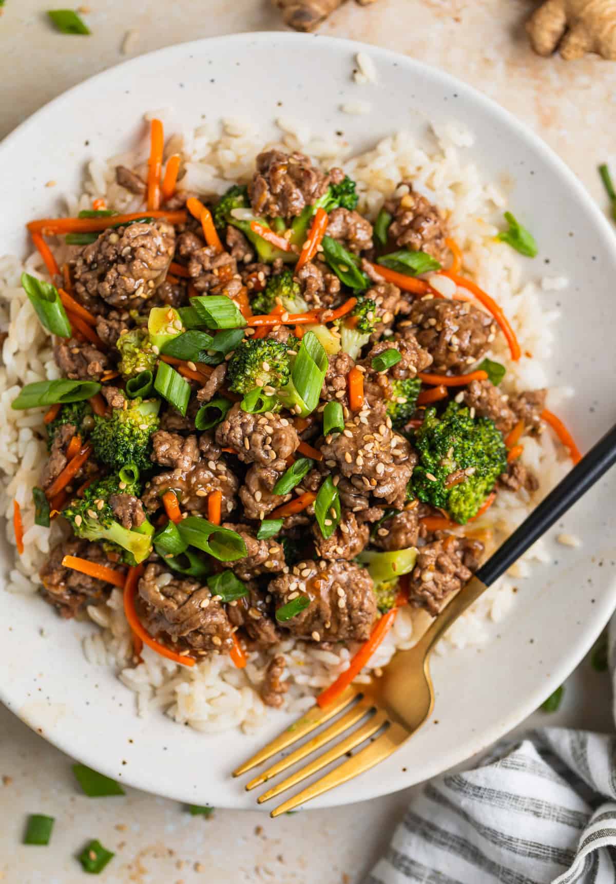 Plate with ground beef teriyaki with broccoli and carrots served over rice and topped with sesame seeds.