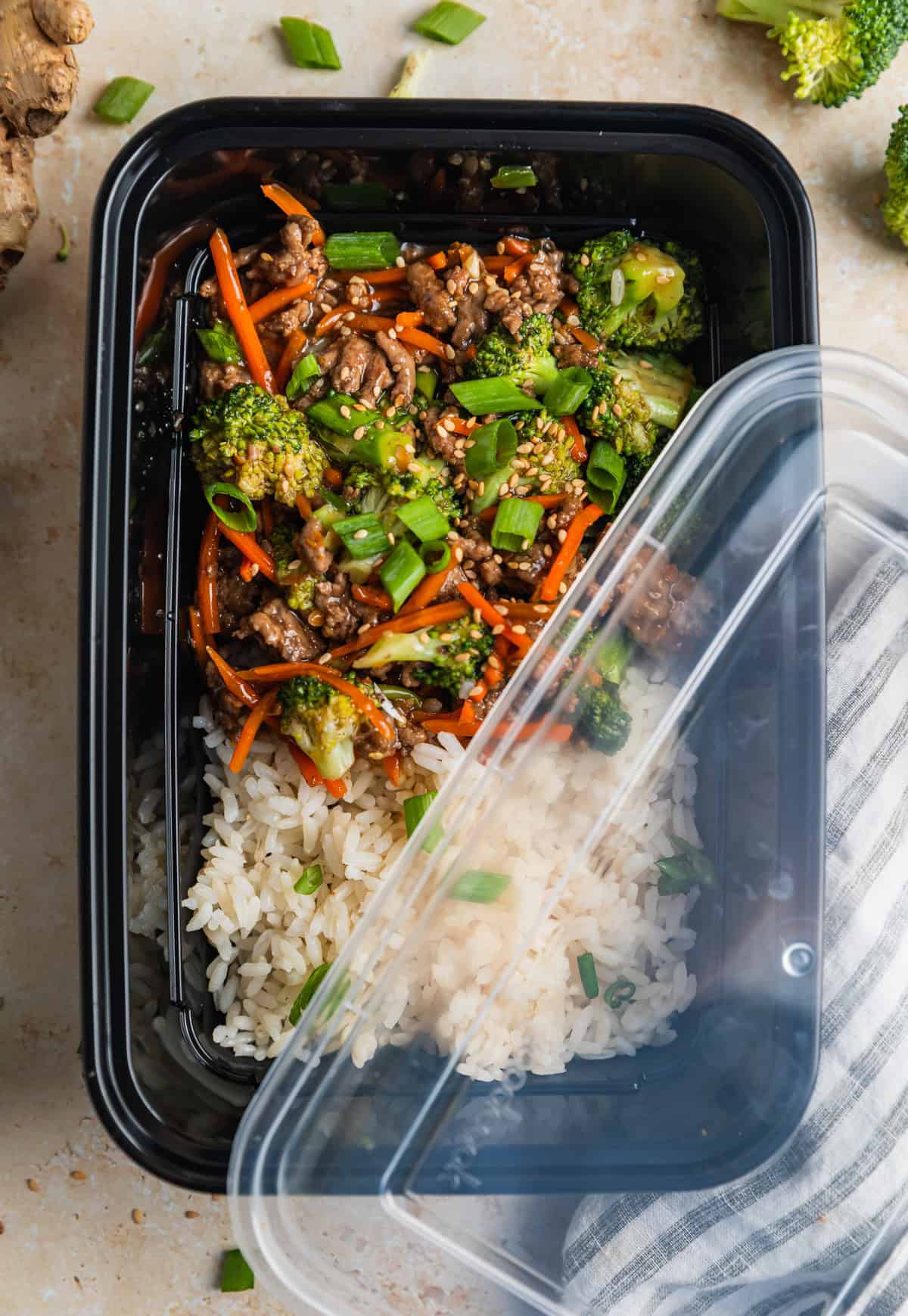 Meal prep container with rice and ground beef teriyaki with lid slightly covering it.