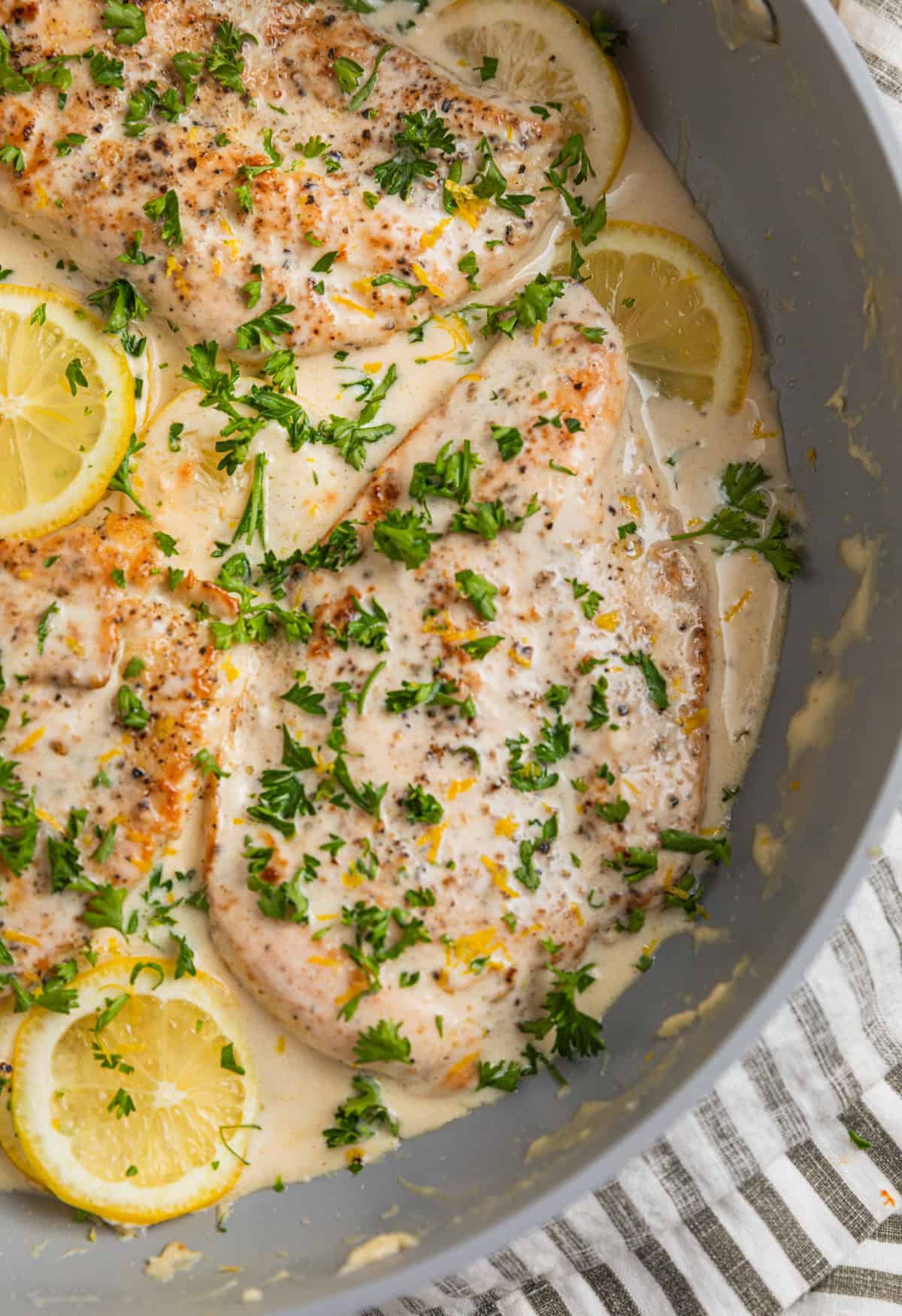 Skillet with creamy lemon chicken topped with chopped parsley.