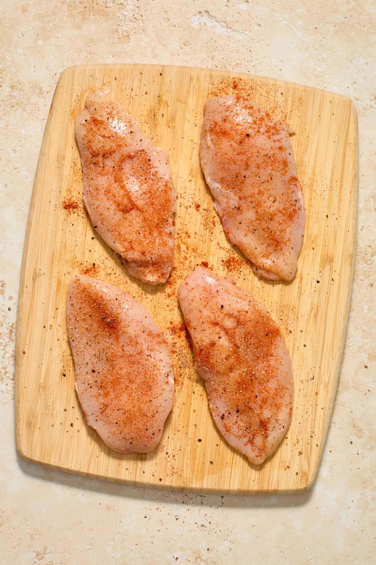 Pounded seasoned chicken breasts on cutting board.