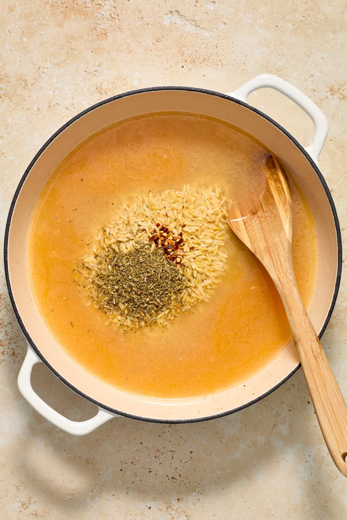 Orzo, broth and seasoning added to pan with wood spoon.