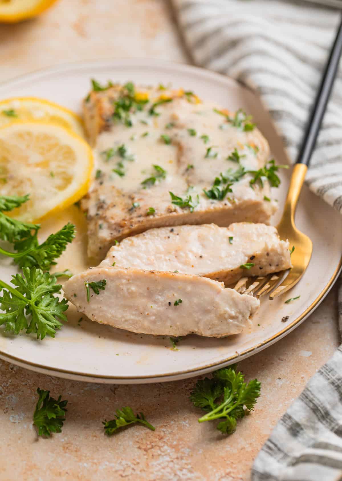 Sliced chicken breast on plate with lemon slices and parsley beside it.