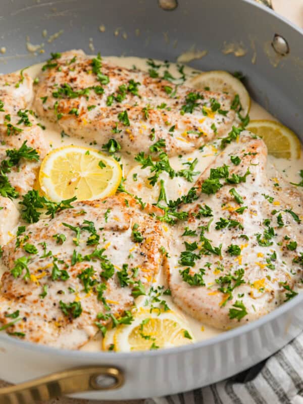 Creamy lemon chicken in skillet with lemon slices, cream cheese sauce and chopped parsley over top.