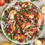 Apple and arugula salad in bowl with toasted maple pecans, goat cheese, dried figs and balsamic dressing.