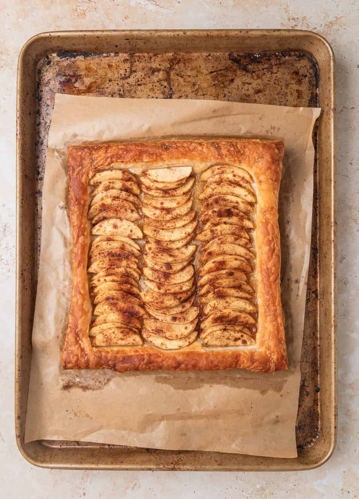 Baked apple and puff pastry tart on baking sheet after baking.