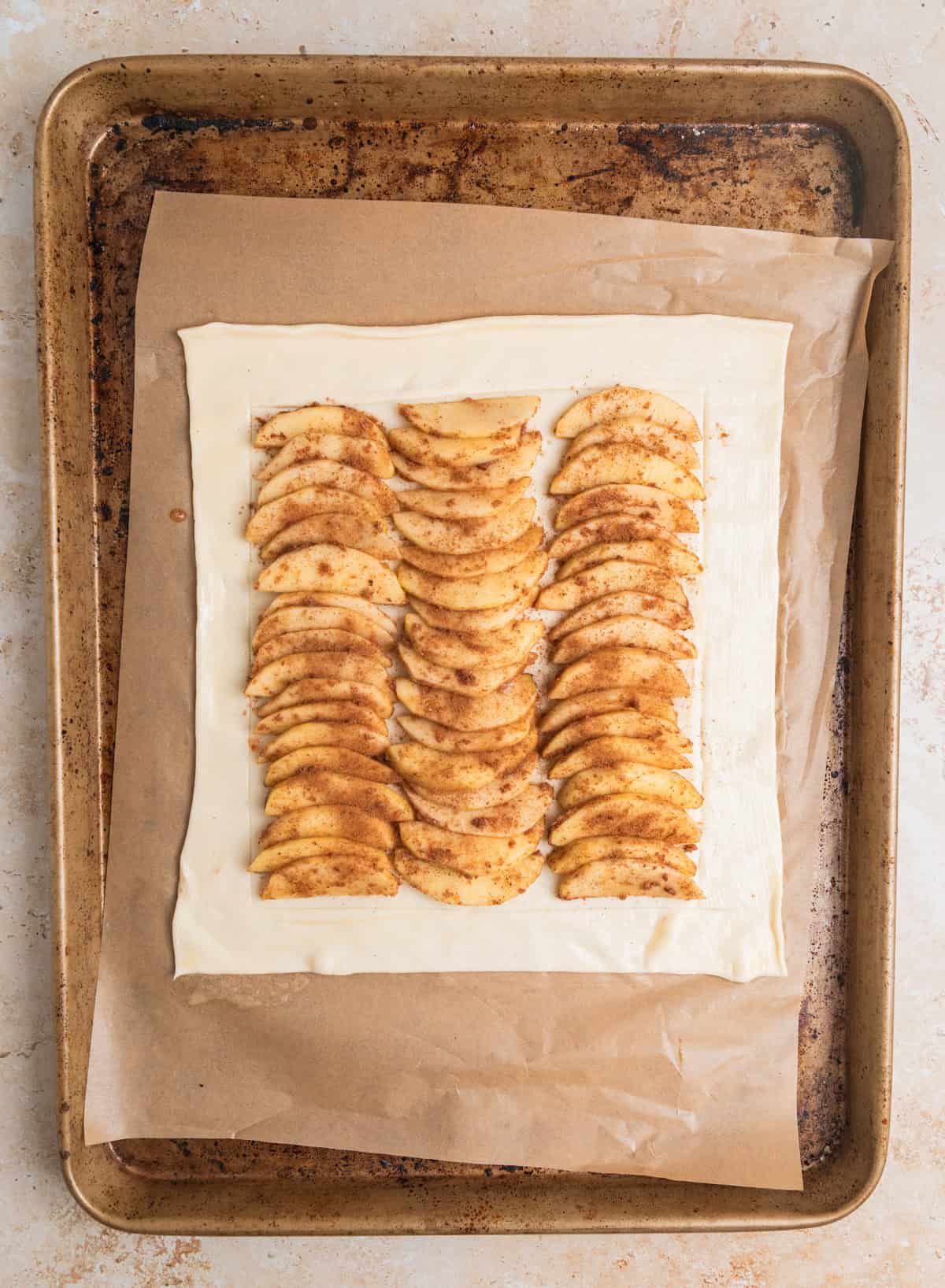 Apple slices lined on scored puff pastry sheet.