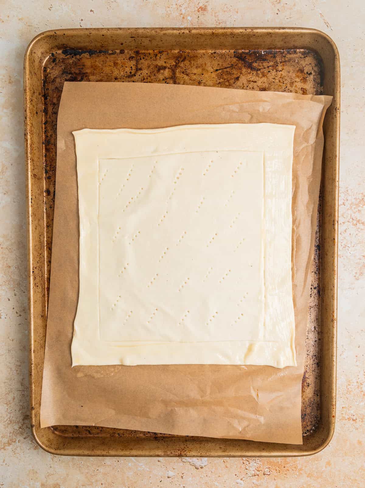 Sheet of puff pastry with edges scored laying on parchment lined sheet pan.