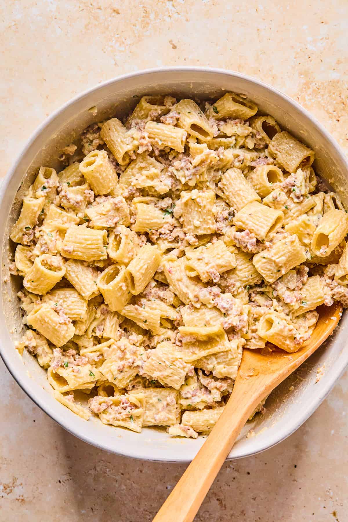 Meat and pasta added to cheese mixture in bowl.