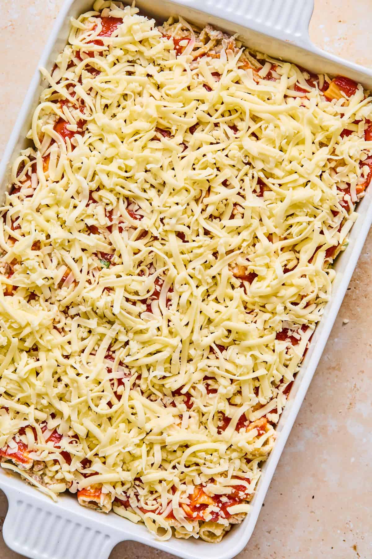 Shredded mozzarella covering top of pasta bake in pan before cooking.