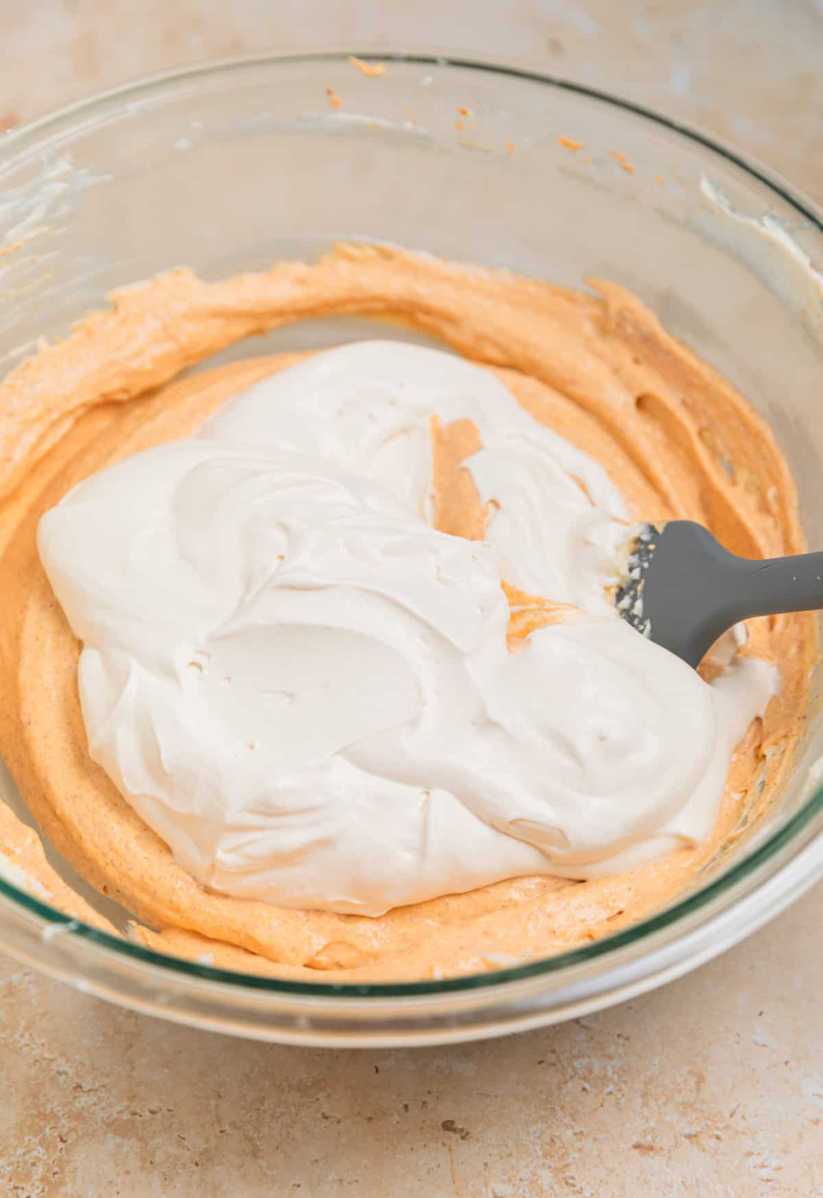 Whipped cream added to pumpkin cream cheese mixture in bowl with spatula. 