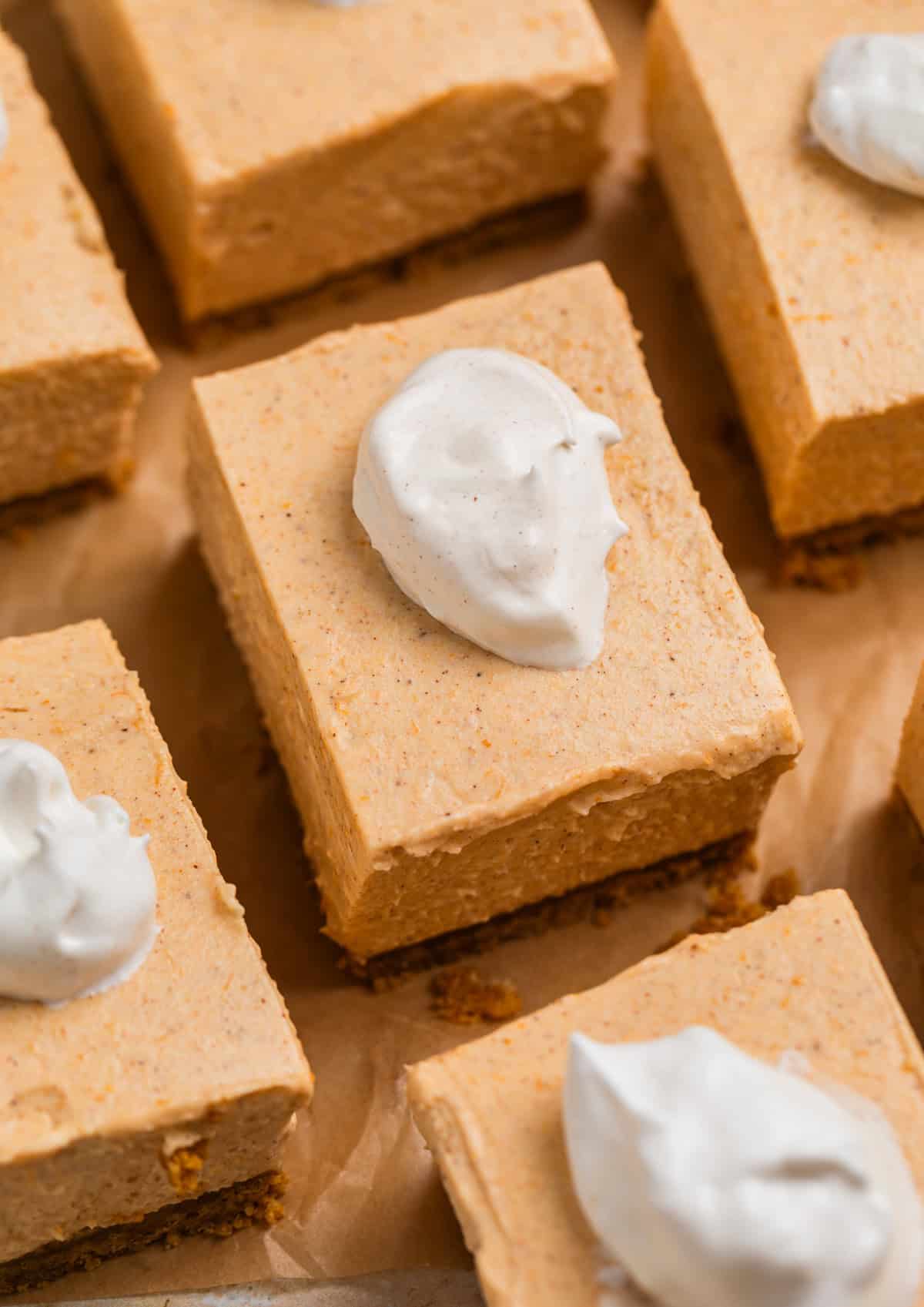 No bake pumpkin cheesecake bars on parchment topped with a dollop of whipped cream.