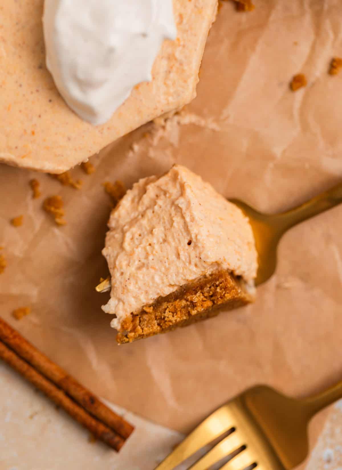 Fork with piece of pumpkin cheesecake resting on it and cinnamon stick and fork surrounding.