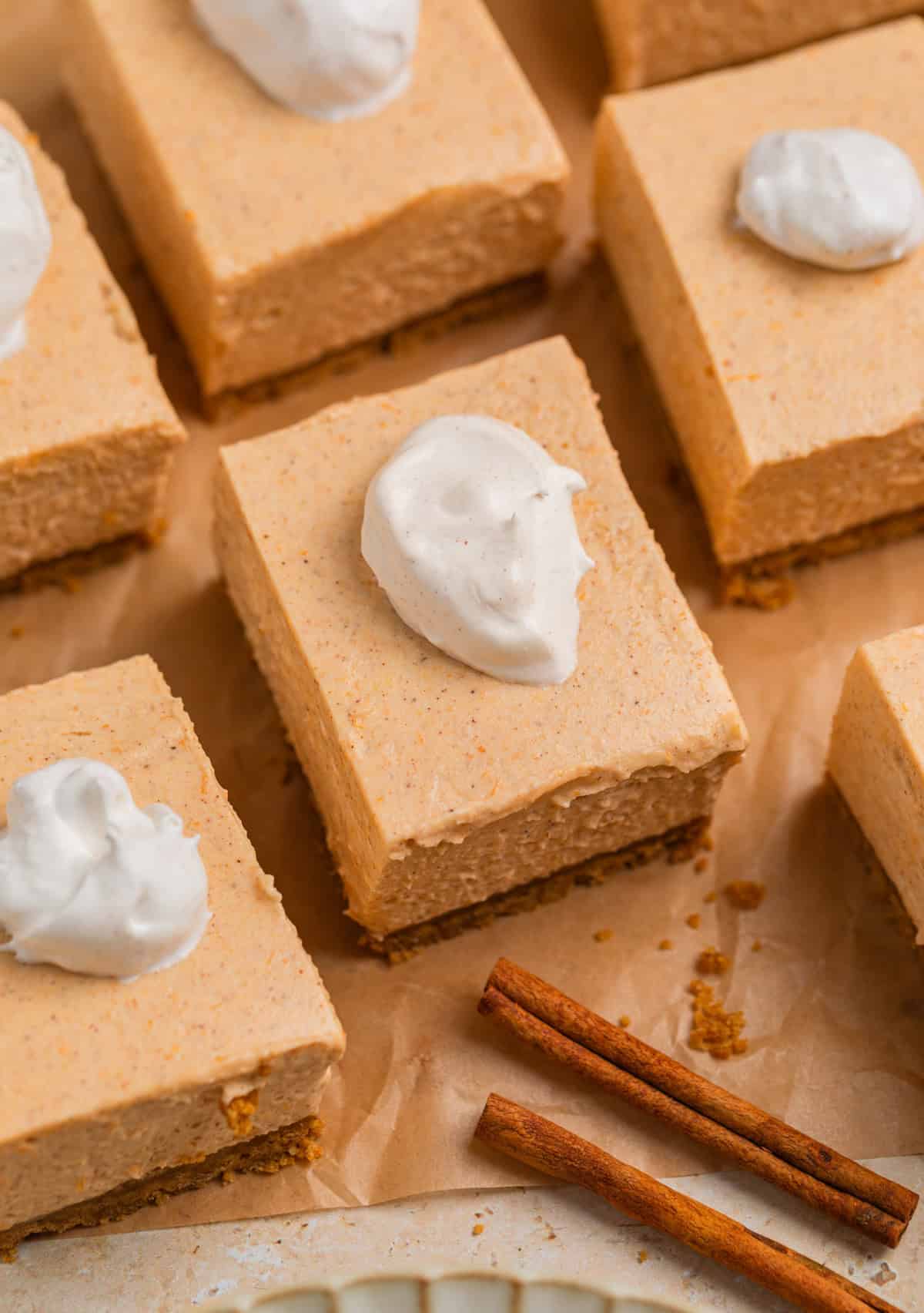 Slices of no bake pumpkin cheesecake on parchment with dollop of whipped cream on top.