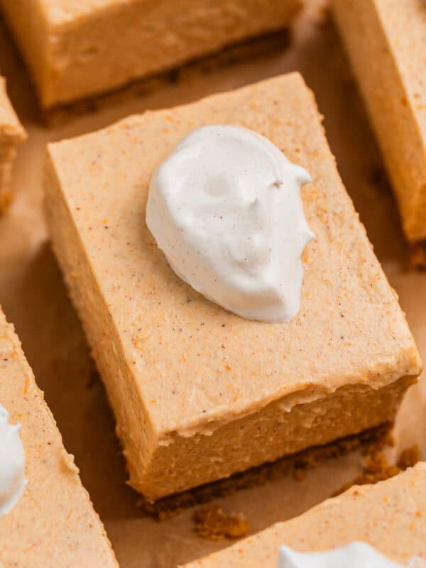 Pumpkin cheesecake bars arranged on brown parchment topped with a dollop of whipped cream.