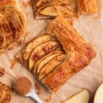 Overhead view of apple tarts on parchment with spoonful of cinnamon beside.