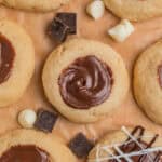 Nutella cookies arranged on parchment with white and dark chocolate chips arranged around the cookies.