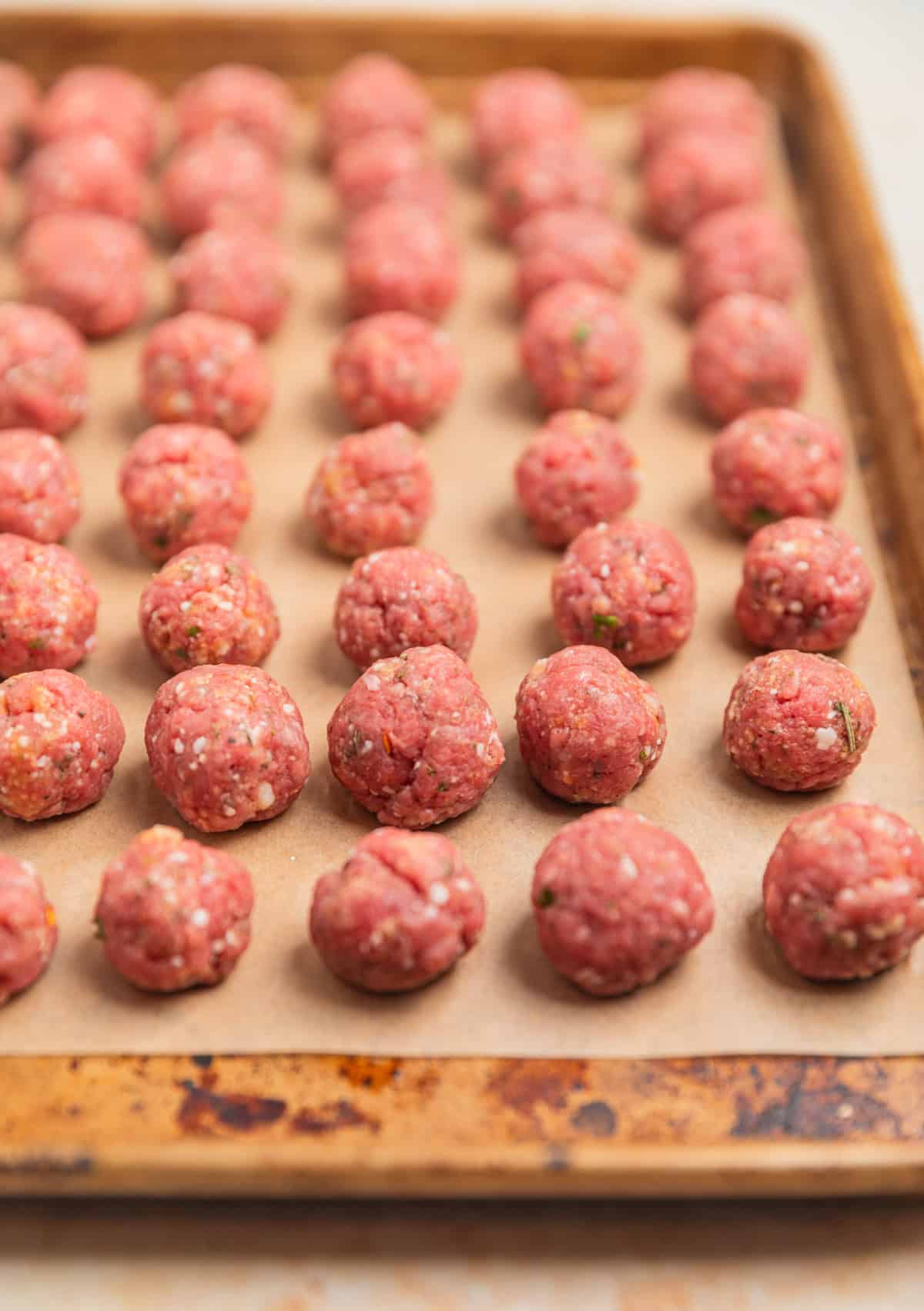Meatballs rolled and arranged on parchment lined pan before being cooked.