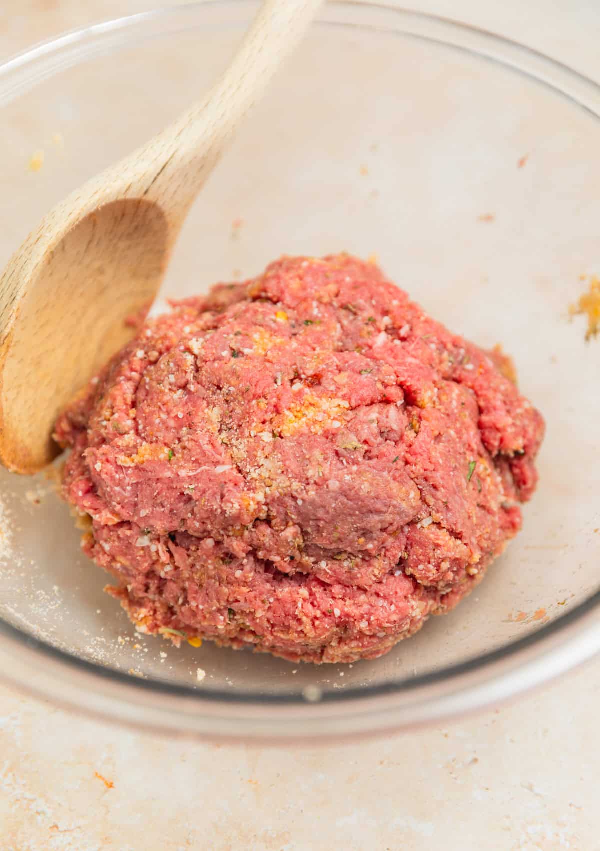 Meatball mixture prepared in bowl with wooden spoon.