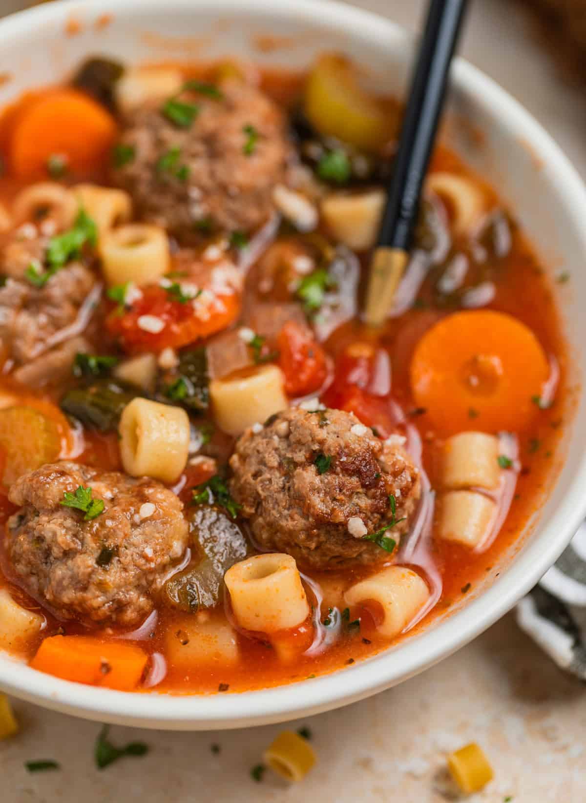 Spoon scooping into bowl with meatball soup topped with grated parmesan and parsley.