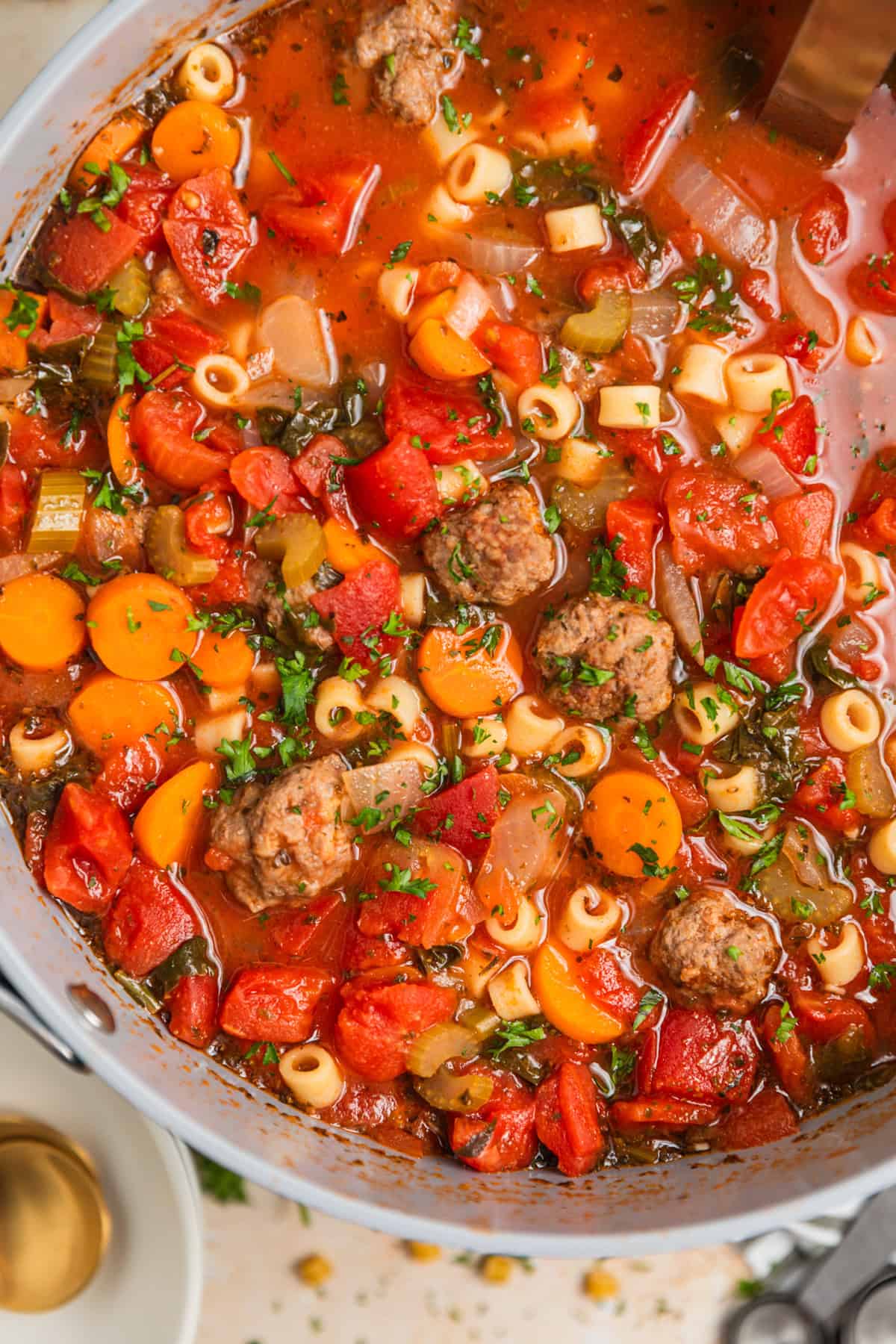 Pot of meatball soup with vegetables, pasta and topped with chopped parsley.