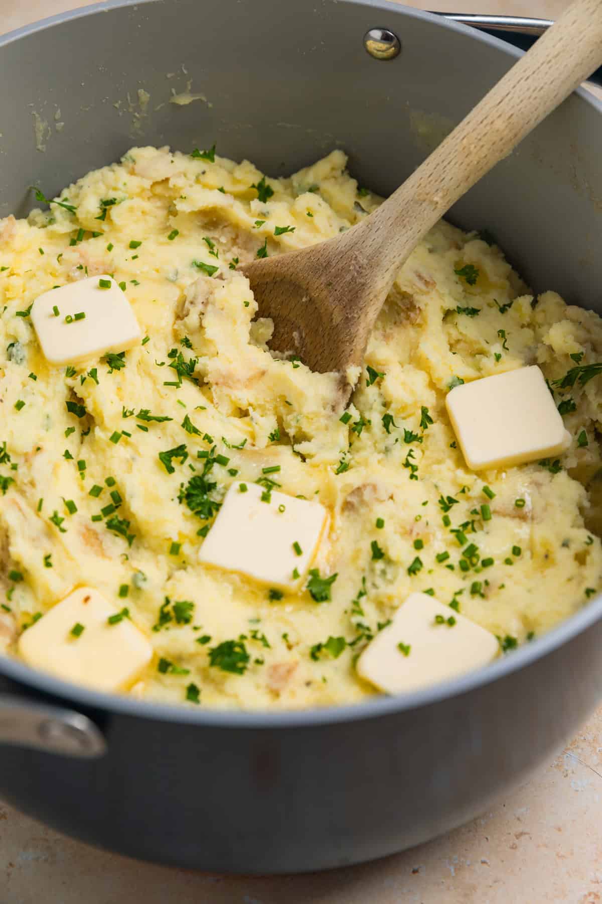 Pot with prepared mashed potatoes topped with fresh chives, parsley and pats of butter.