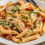 White plate with creamy chicken pasta and fresh herbs on top.