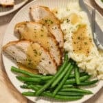 Slices of turkey breast on plate with mashed potatoes and green beans.
