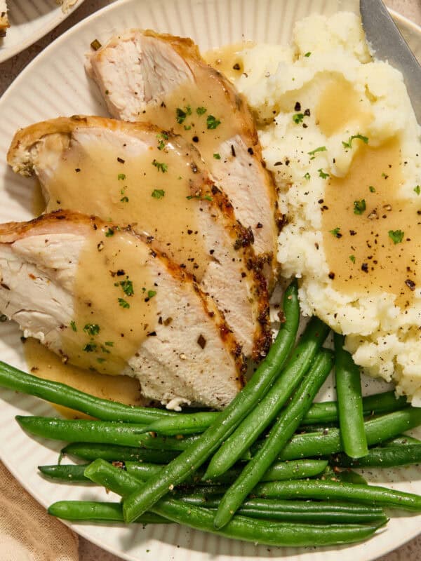 Slices of turkey breast on plate with mashed potatoes and green beans.