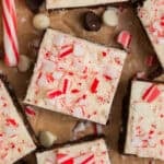 Brownies topped with white chocolate peppermint bark with candy canes and white and dark chocolate chips around them.