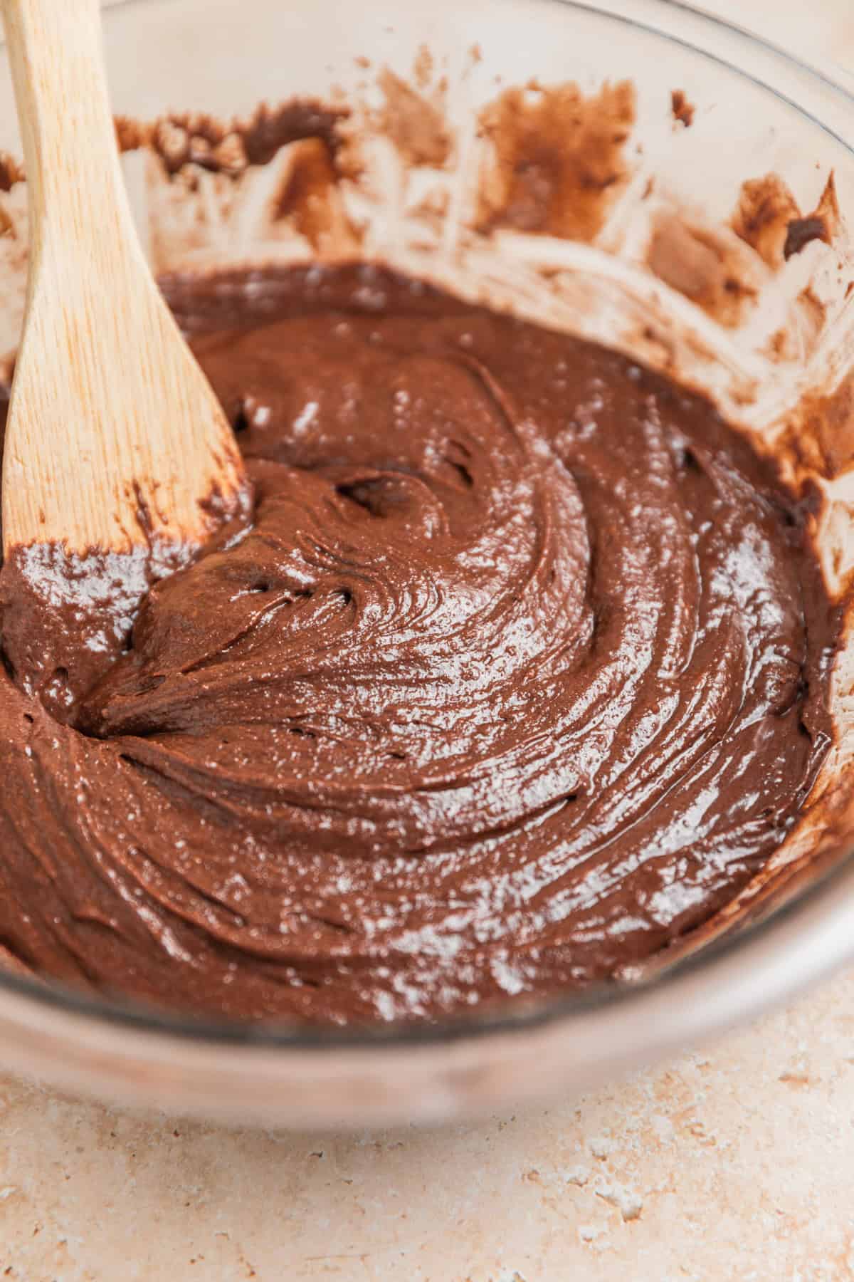 Brownie batter in glass bowl with wooden spoon.