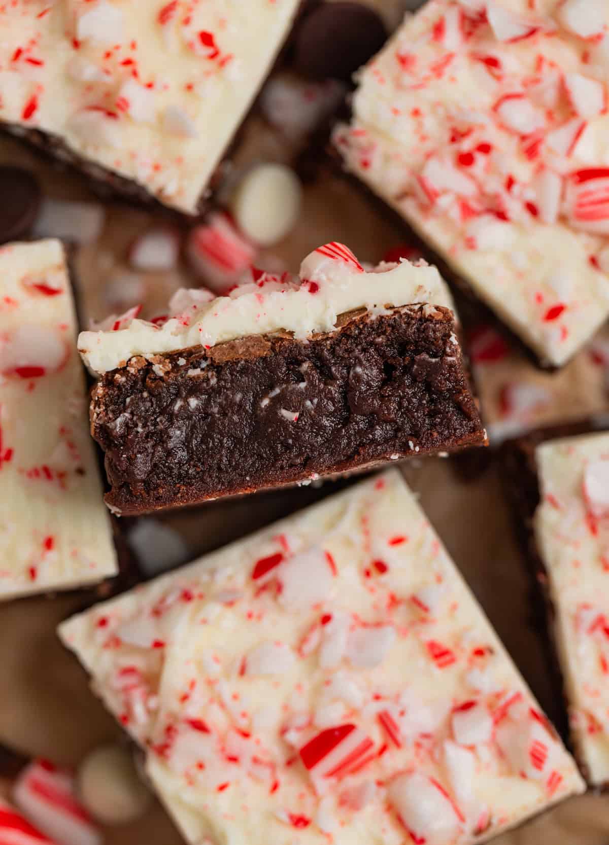 Peppermint bark topped brownies arranged on parchment with one propped on its side to show layers.