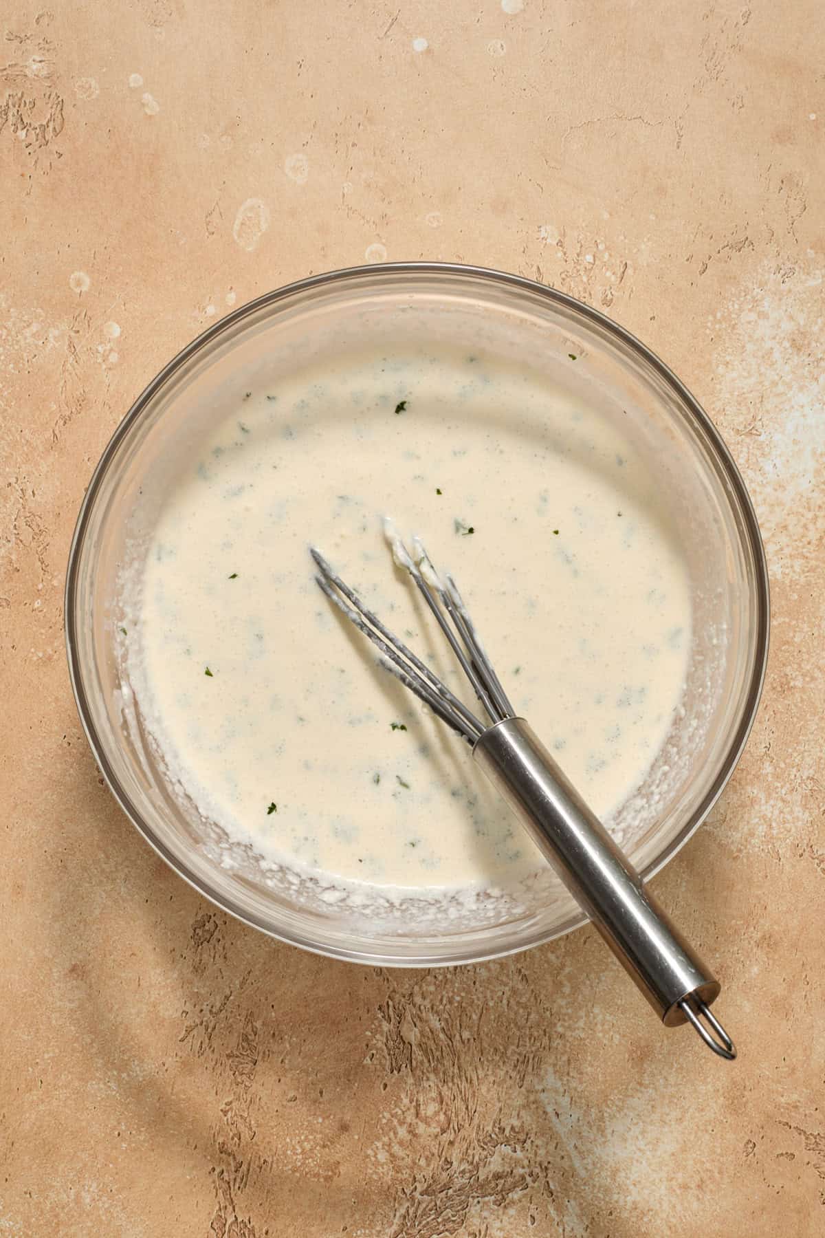 Creamy parmesan mixture in bowl with whisk.