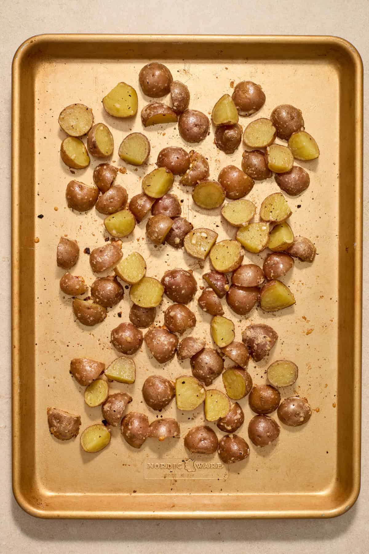 Partially roasted parmesan potatoes on pan.