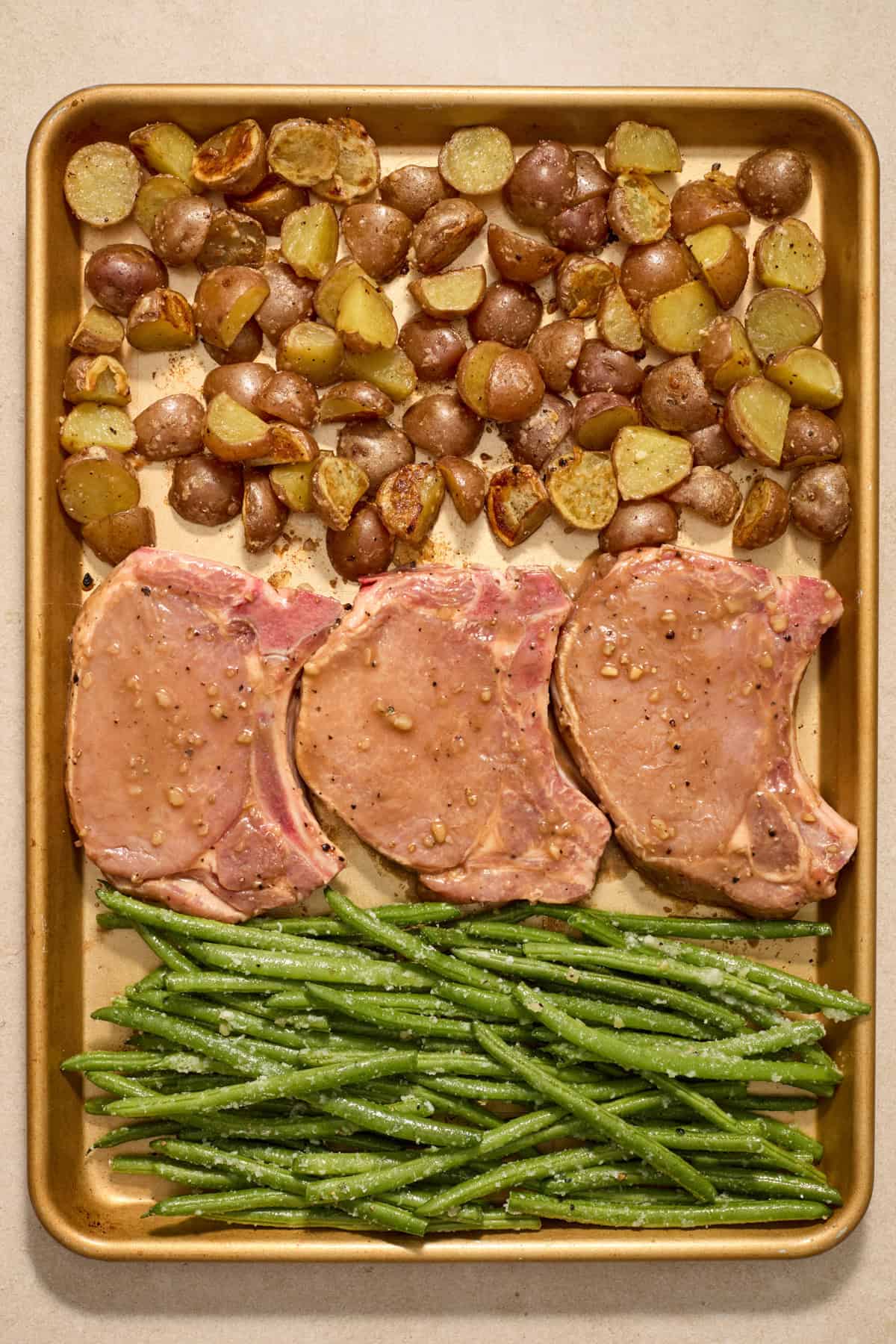 Baking sheet with potatoes, pork chops and green beans before being placed in oven.