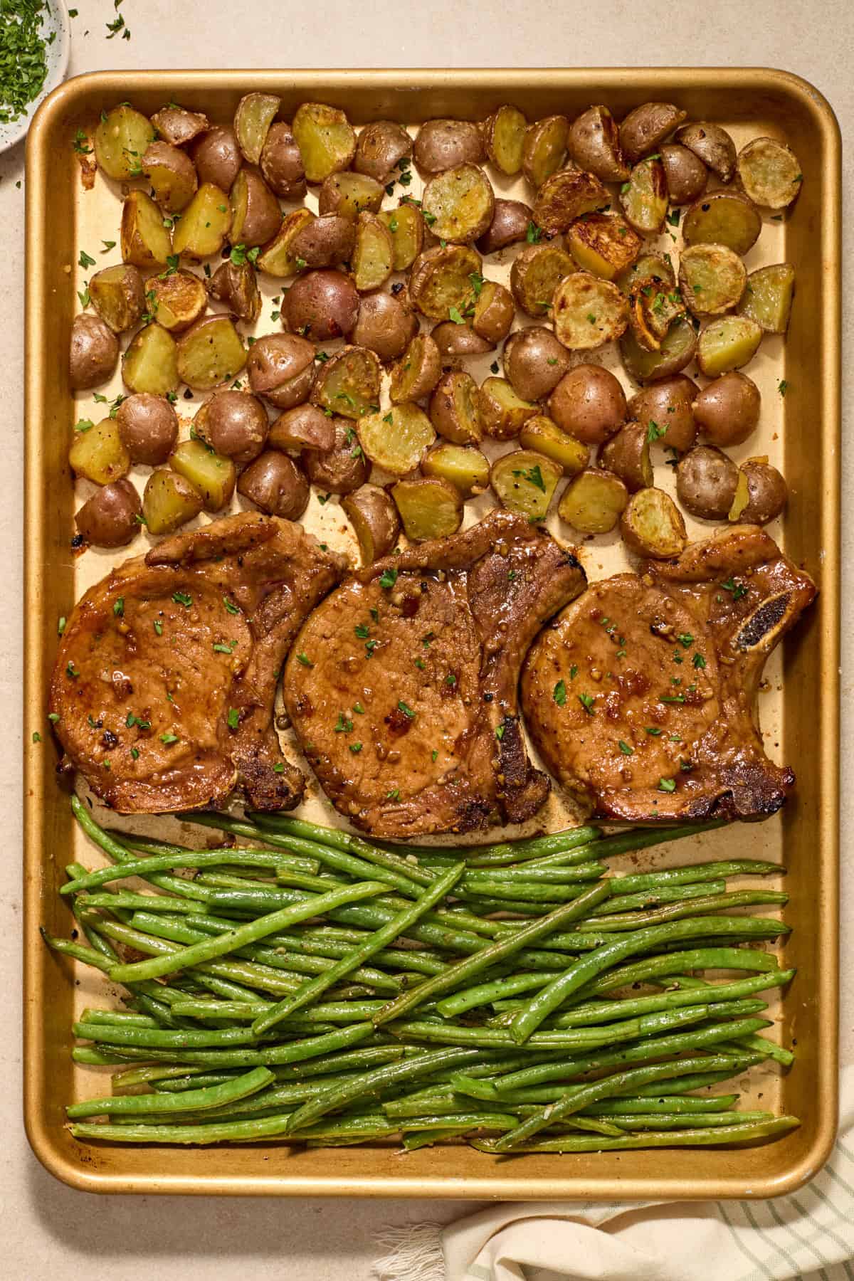 Sheet pan pork chops with parmesan potatoes and green beans on pan.