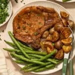 Sheet pan pork chops served on plate with potatoes and green beans.
