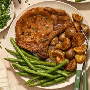 Sheet pan pork chops served on plate with potatoes and green beans.