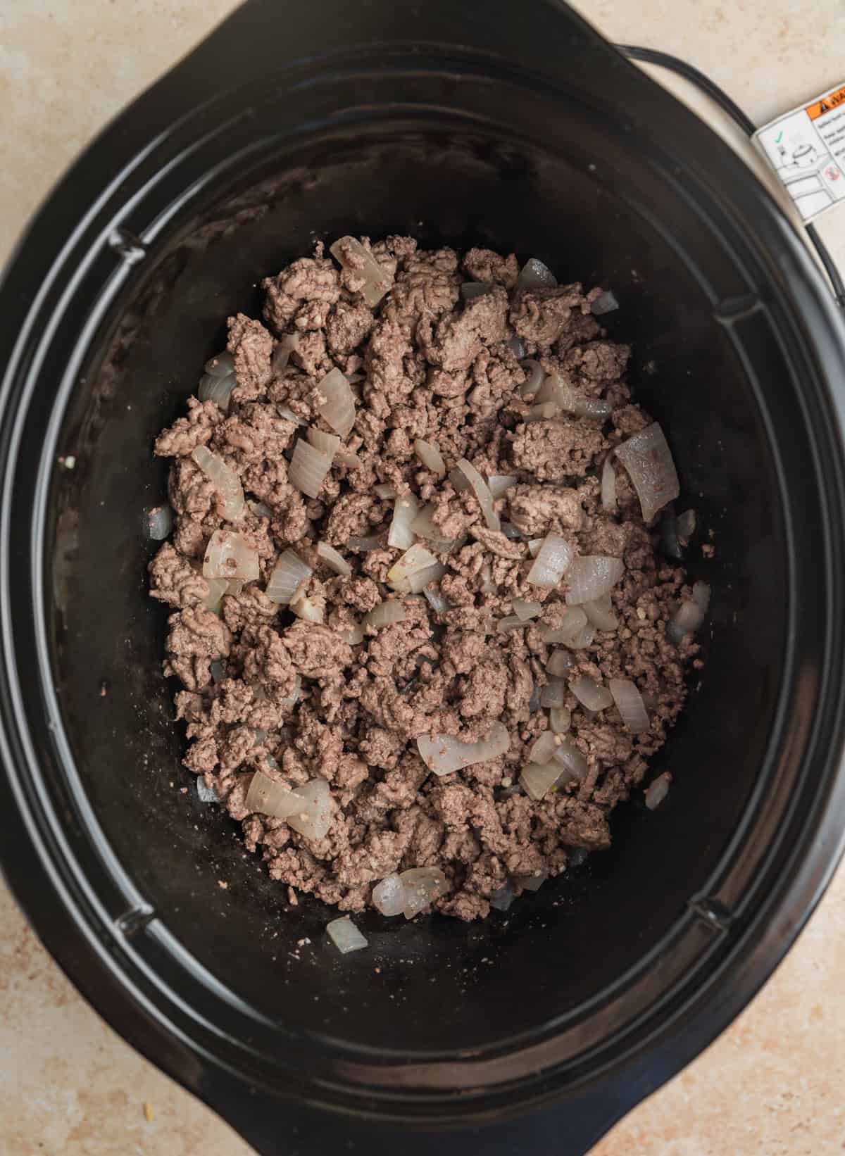 Crock pot with browned beef and sautéed onions at the bottom.