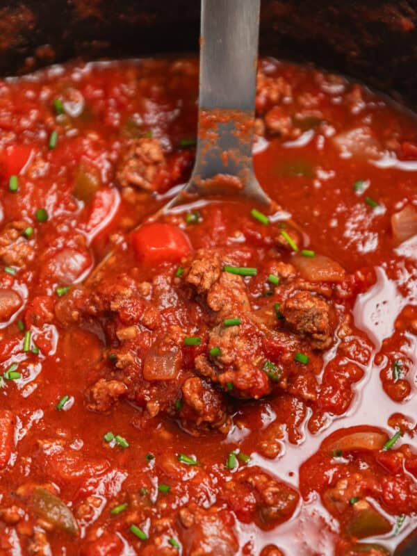 Crock pot with beef chili being scooped up in a ladle.